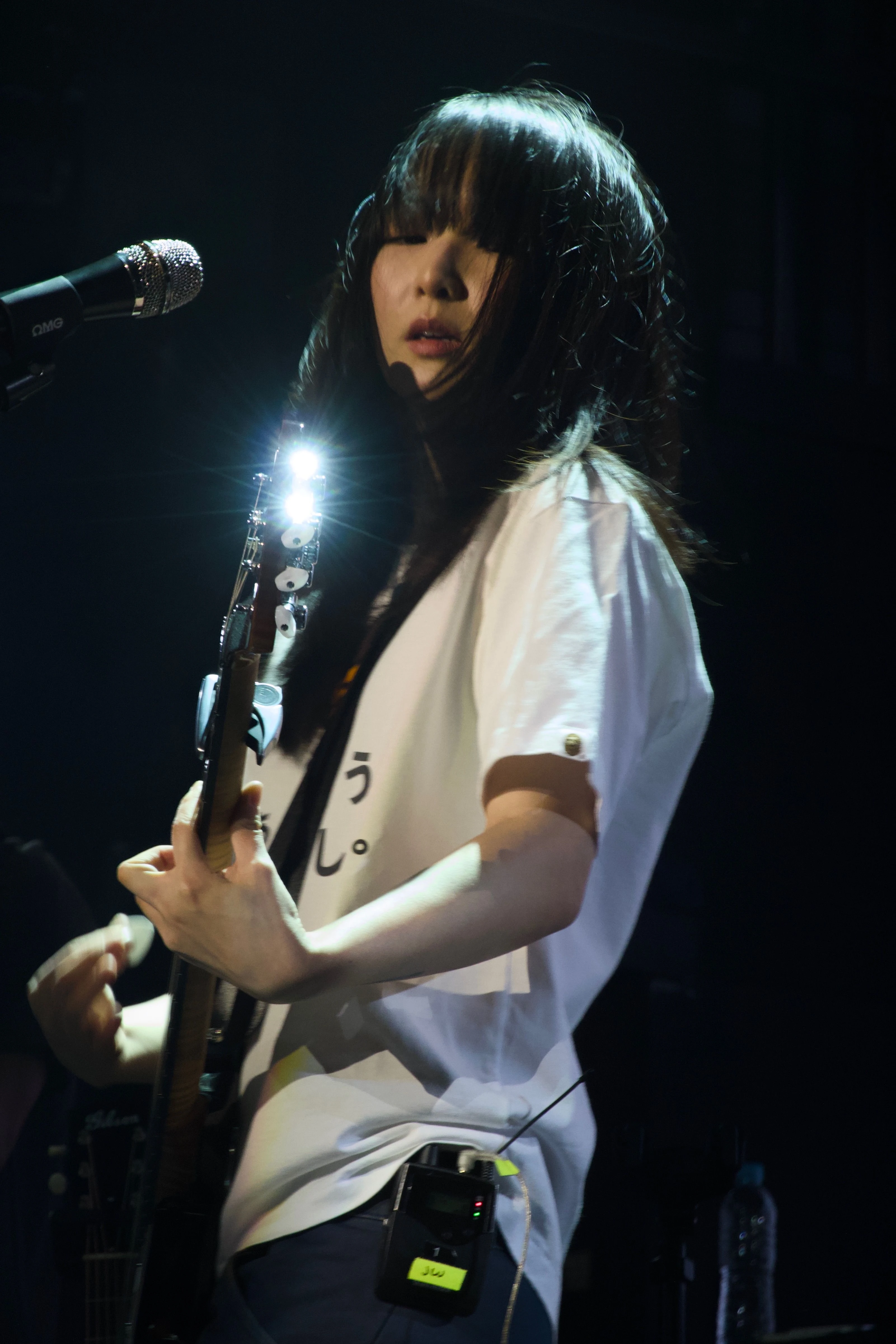 일렉트릭 기타를 연주하는 정우의 모습. 기타 끝의 머신 헤드가 무대 조명을 반사해 반짝이고 있다.