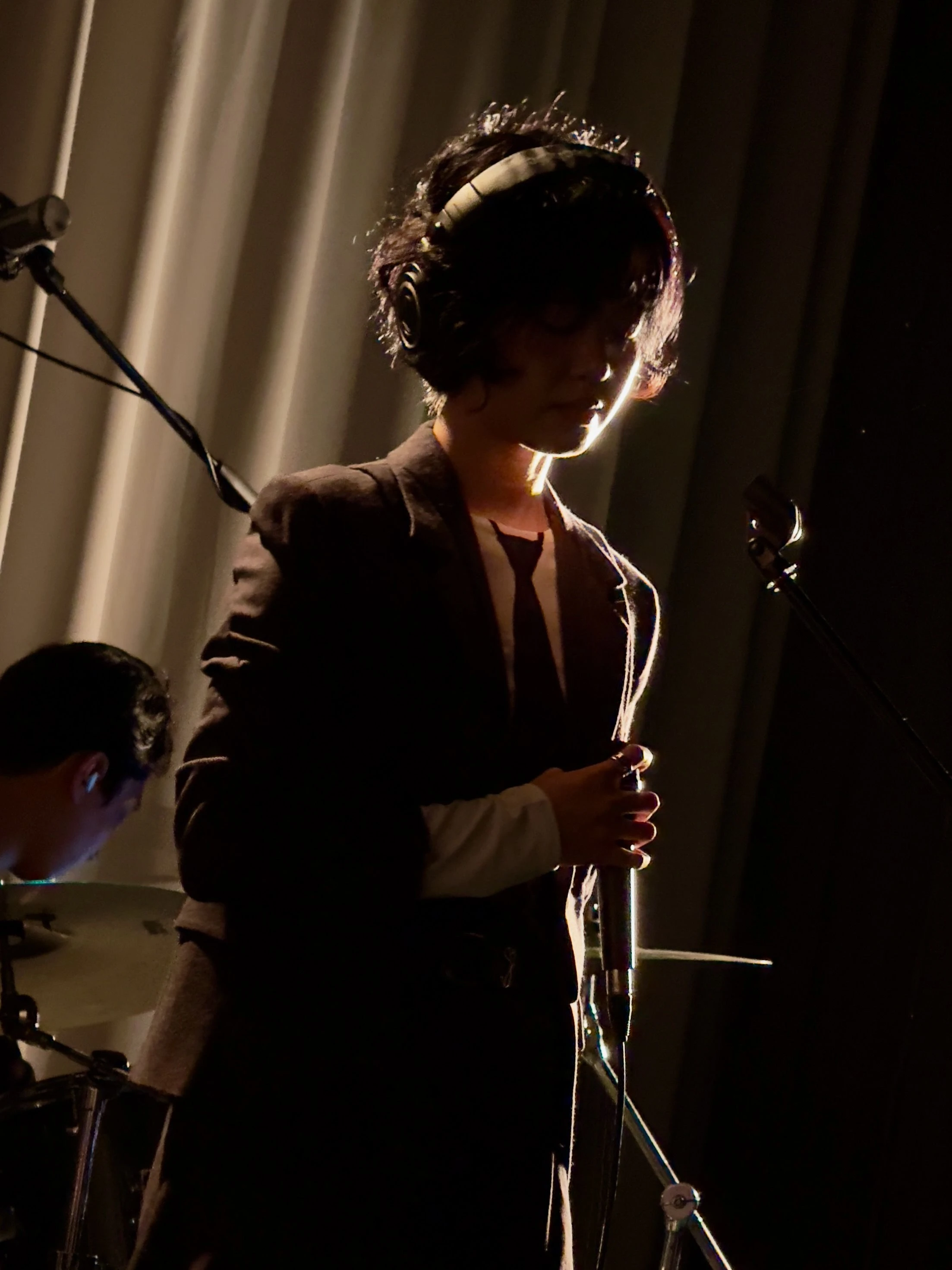 가수 윤지영이 마이크를 잡으며 눈을 감고 있다. 무대 조명은 그의 측면을 비추고 있다.