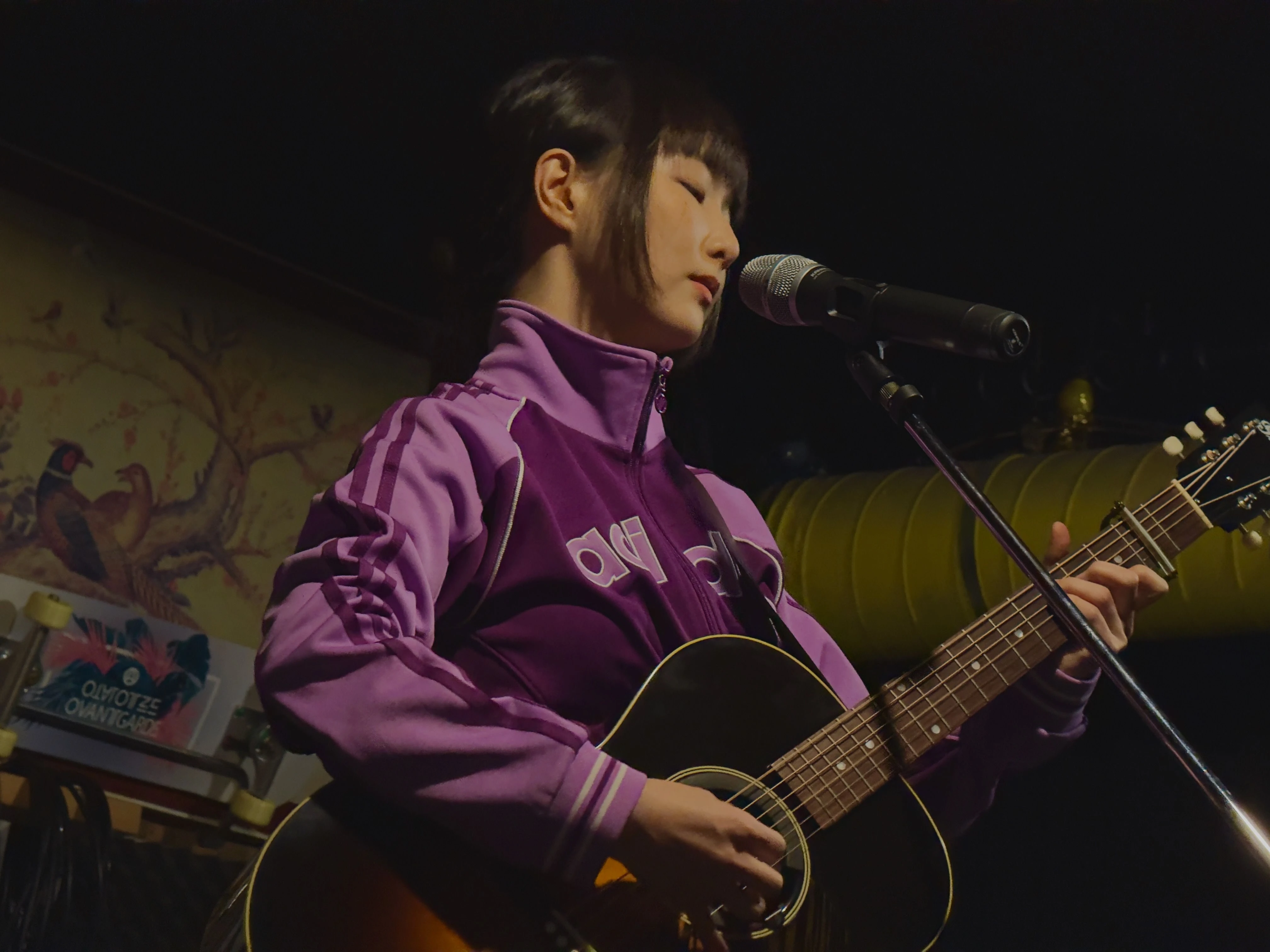 트레이닝 복을 입은 가수 정우가 마이크 스탠드 앞에서 어쿠스틱 기타를 연주하고 있다.