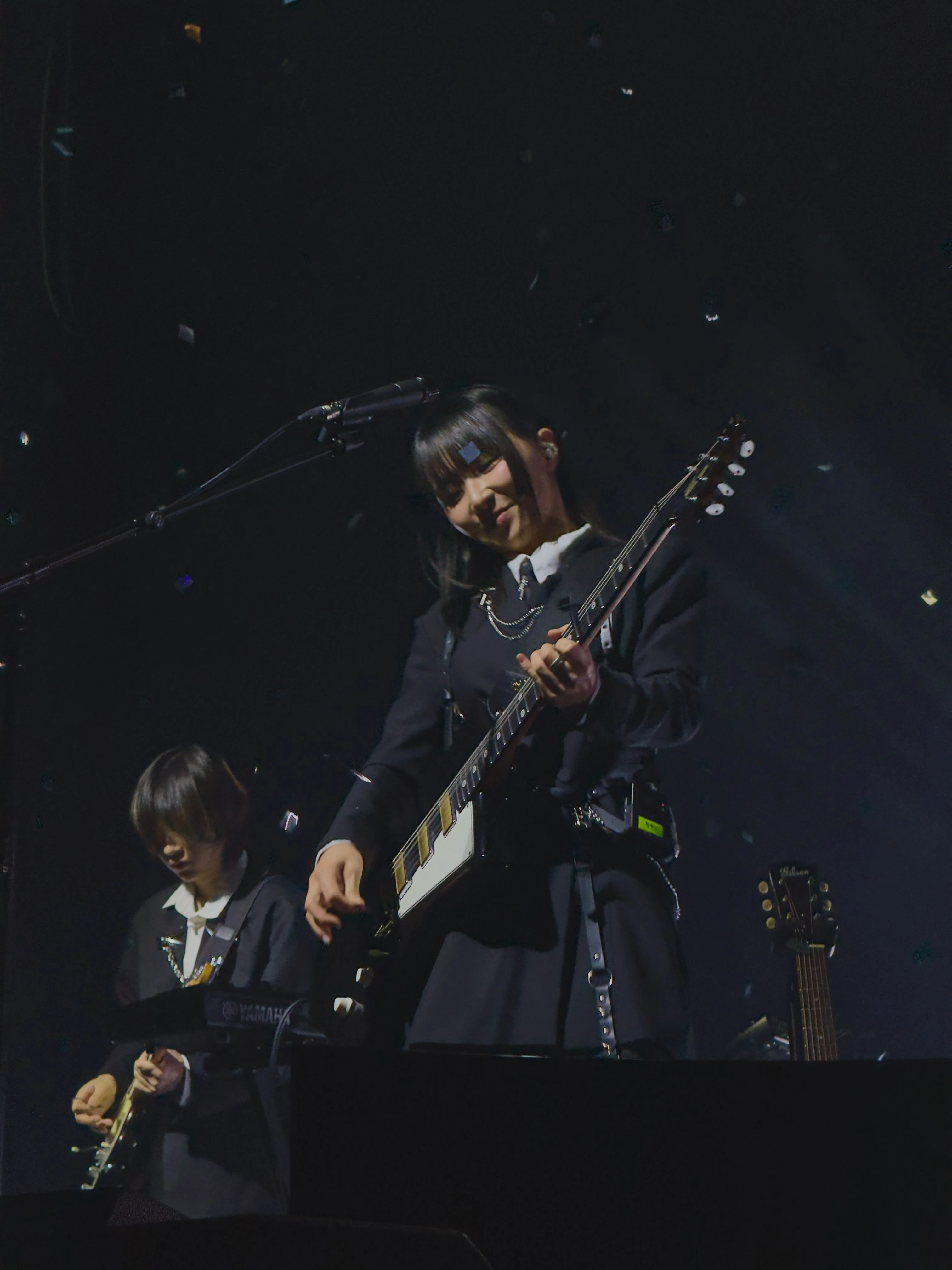 가수 정우가 무대에서 시선을 아래로 향한 채로 웃으며 일렉트릭 기타를 연주하고 있다. 무대 위에서는 컨페티가 떨어지고 있다. 