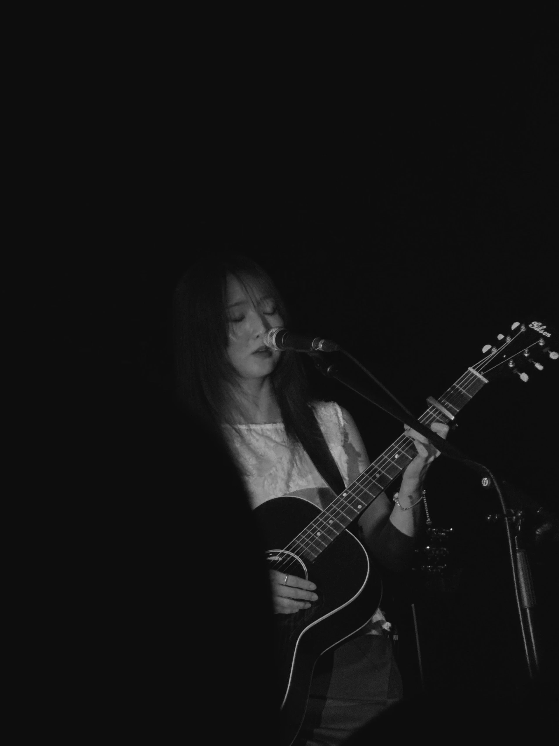 정우가 어쿠스틱 기타를 연주하면서 마이크 스탠드 앞에서 눈을 감고 노래를 부르고 있다.