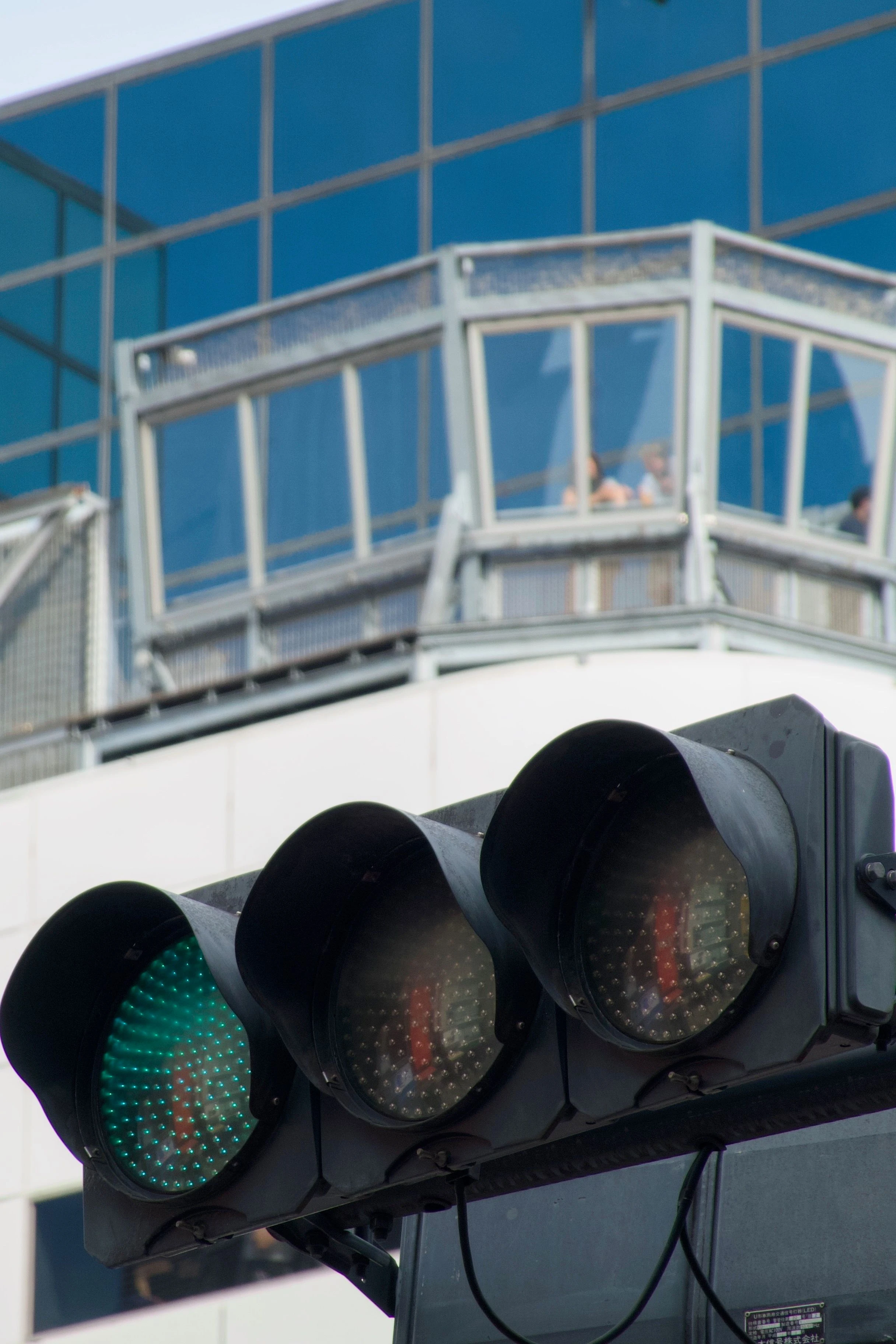 초록색 신호등에 초점이 맞춰져 있고, 그 너머에는 건물 전망대에 사람들이 서 있는 모습이 보인다.