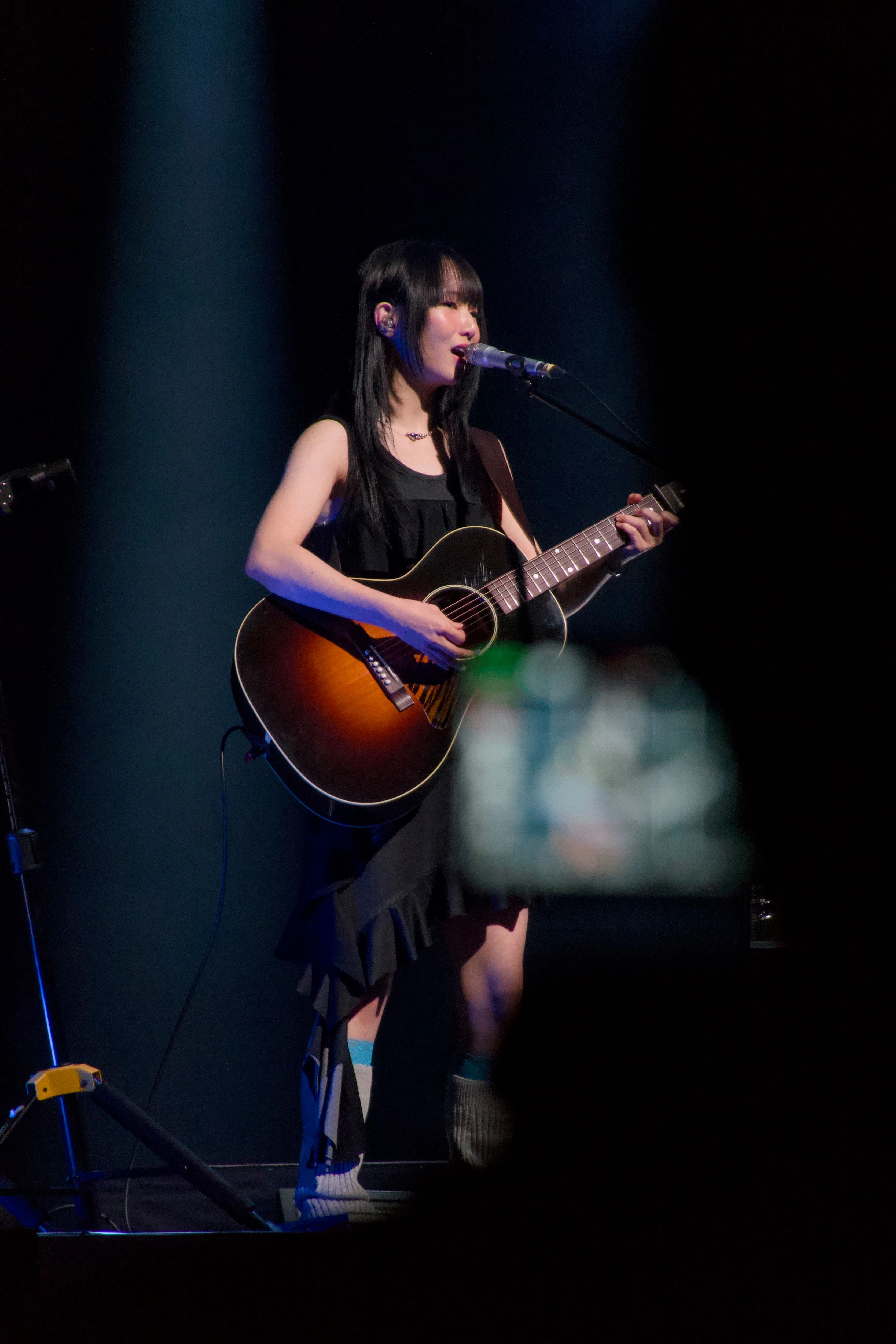 정우가 어쿠스틱 기타를 연주하며 노래를 부르고 있다. 관객석에는 그의 모습을 촬영하는 카메라의 디스플레이가 보인다.