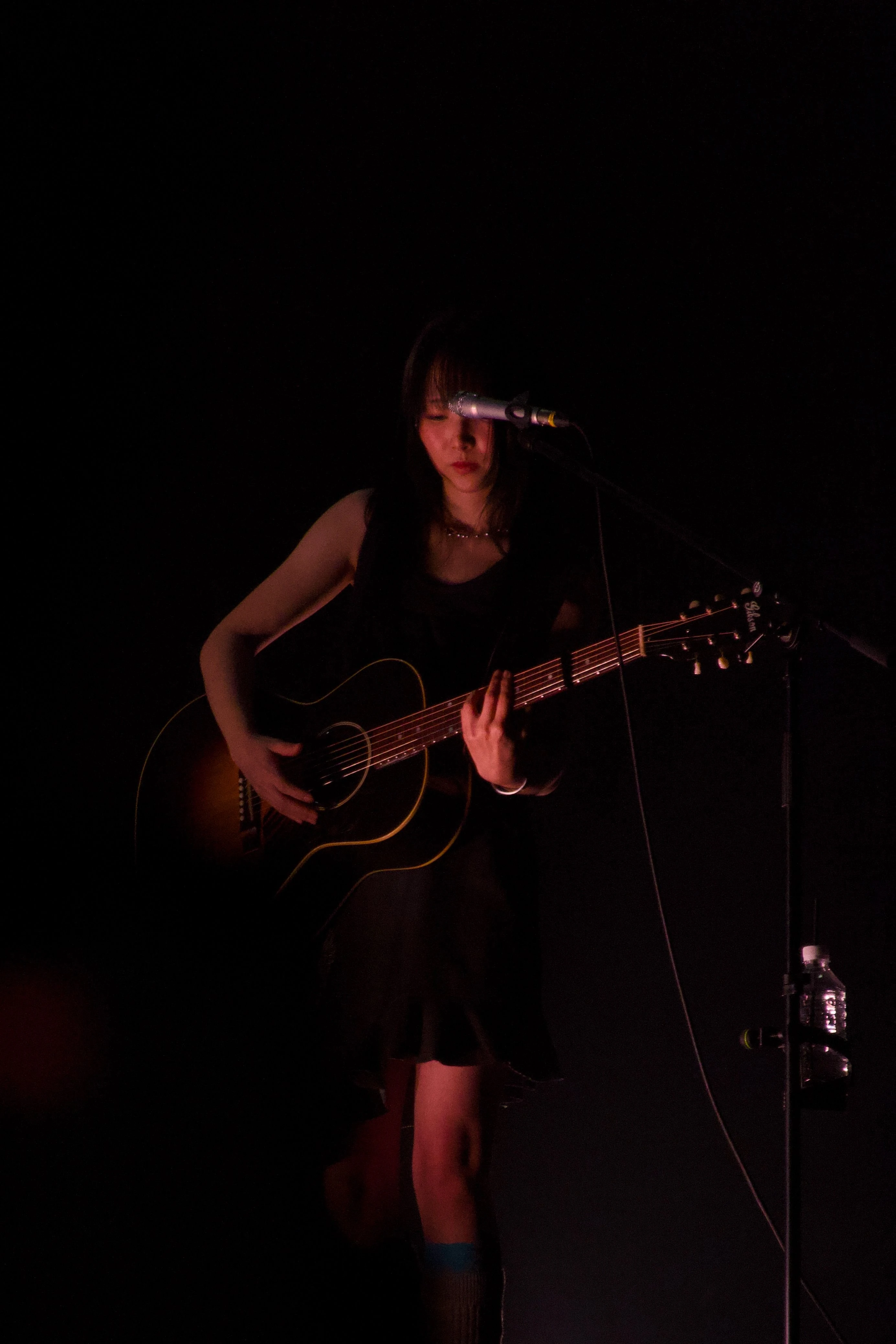 어둡고 붉은 조명 아래 정우가 어쿠스틱 기타를 연주하고 있다.