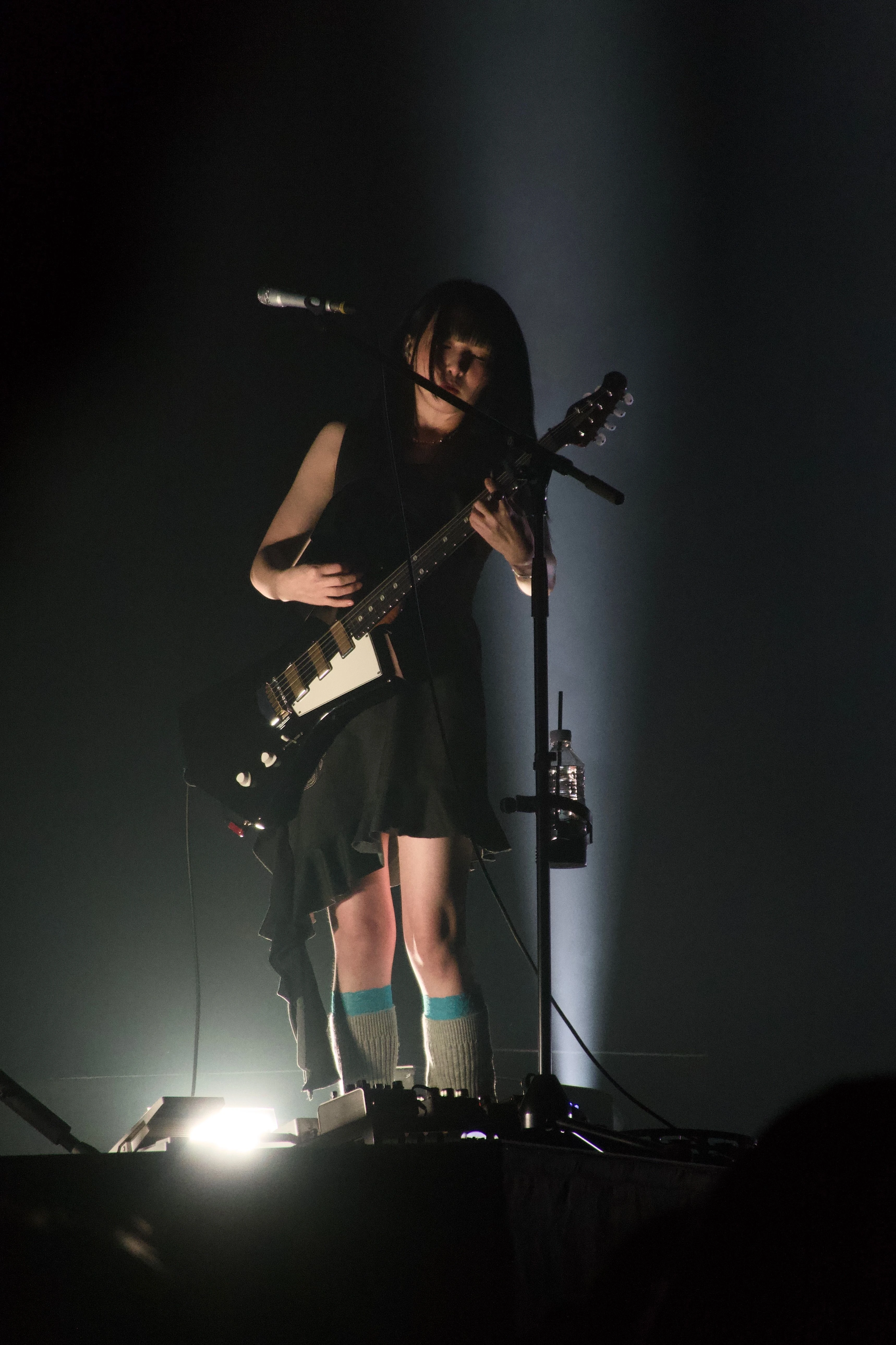 일렉트릭 기타를 연주하는 정우의 모습. 흰색 조명이 무대 아래에서 그를 비춘다.