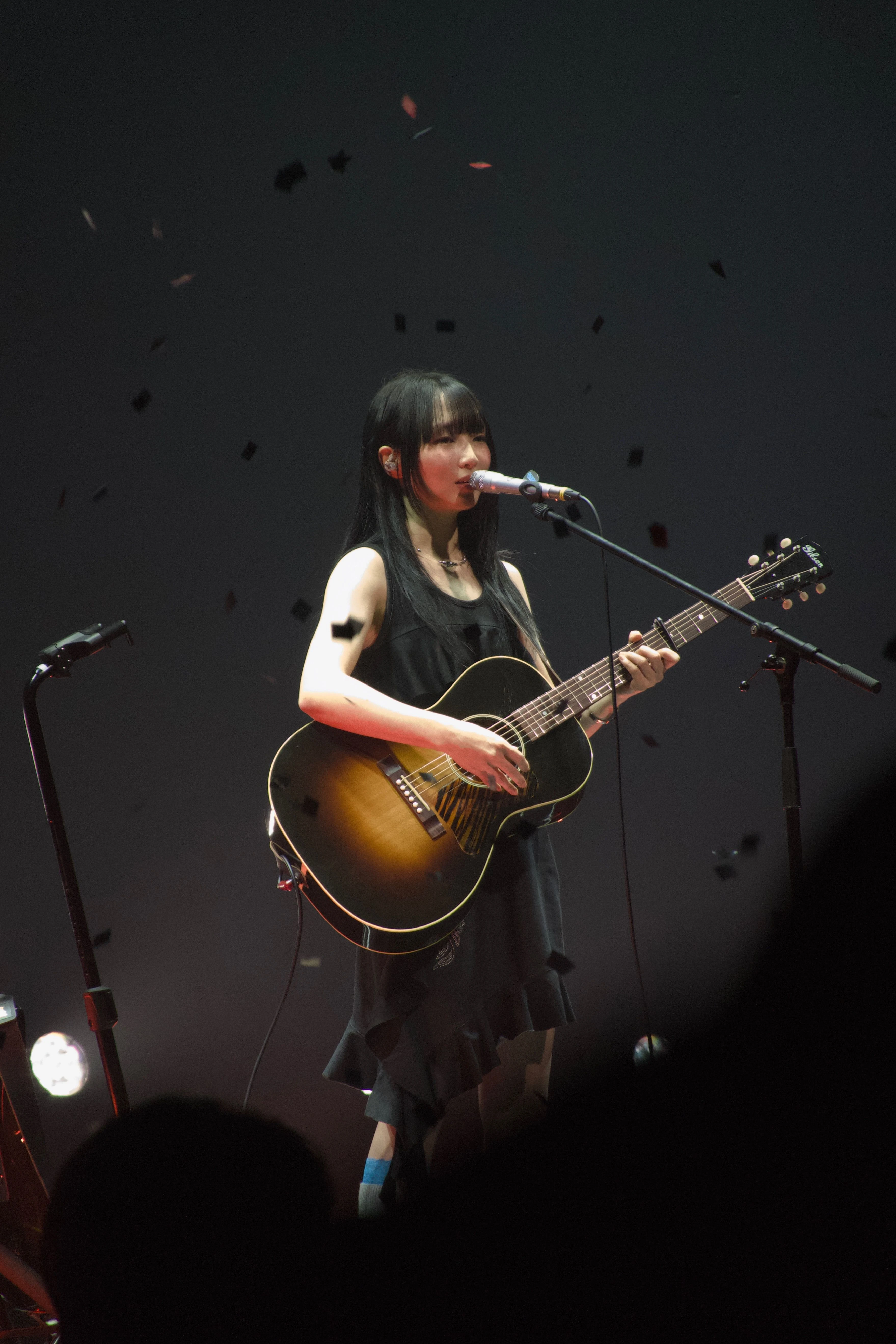 정우가 어쿠스틱 기타를 연주하며 노래를 부르고 있다. 무대 위에서는 컨페티가 떨어지고 있다.