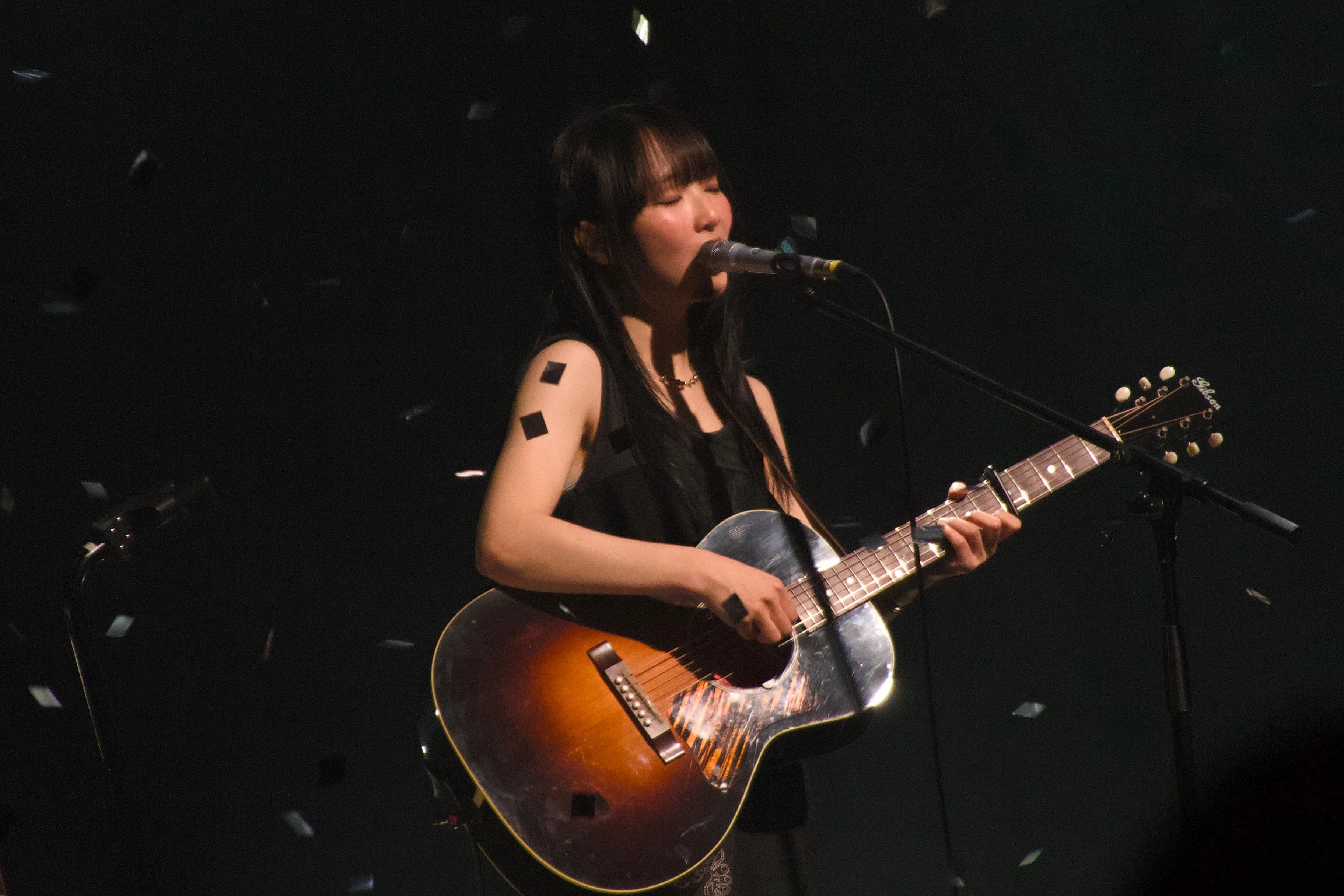 정우가 어쿠스틱 기타를 연주하며 눈을 감은 채로 노래를 부르고 있다. 무대 위에서는 컨페티가 떨어지고 있다.