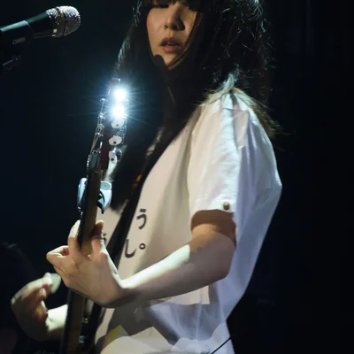 일렉트릭 기타를 연주하는 정우의 모습. 기타 끝의 머신 헤드가 무대 조명을 반사해 반짝이고 있다.