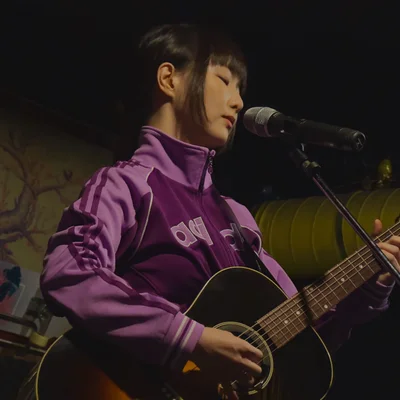 트레이닝 복을 입은 가수 정우가 마이크 스탠드 앞에서 어쿠스틱 기타를 연주하고 있다.