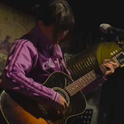 트레이닝 복을 입은 가수 정우가 마이크 스탠드 앞에서 어쿠스틱 기타를 연주하고 있다.