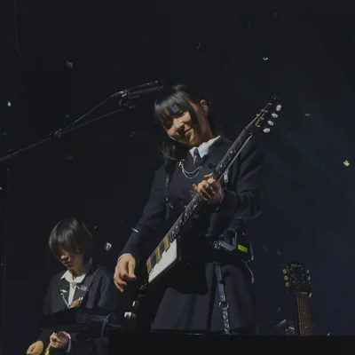 가수 정우가 무대에서 시선을 아래로 향한 채로 웃으며 일렉트릭 기타를 연주하고 있다. 무대 위에서는 컨페티가 떨어지고 있다. 