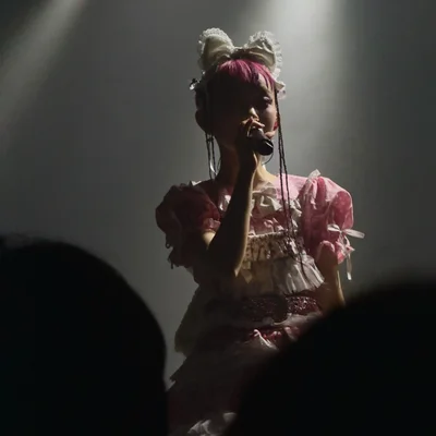 롤리타 패션 복장을 한 WEDNESDAY CAMPANELLA(수요일의 캄파넬라)의 우타하가 마이크를 잡고 노래를 부르고 있다. 무대 조명은 그의 측면을 비추고 있다.