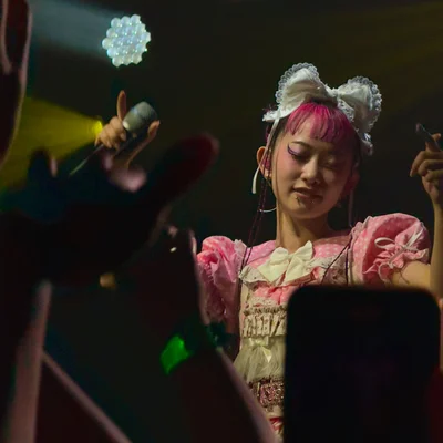 롤리타 패션 복장을 한 WEDNESDAY CAMPANELLA(수요일의 캄파넬라)의 우타하가 눈을 감고 춤을 추고 있다. 객석에는 팔을 뻗은 관객들의 손이 보인다.