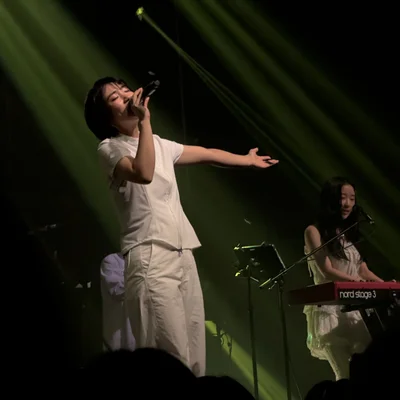 신온유가 오른손에 마이크를 쥐고 노래를 부르면서 왼팔을 옆으로 뻗고 있다. 그의 옆에는 키보드를 연주하는 하형언의 모습이 보인다.