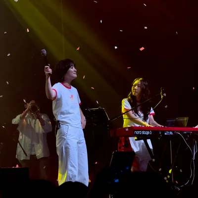 무대 위에서 떨어지는 컨페티 아래 신온유가 마이크를 잡고 위를 향해 들고 있고, 하형언은 키보드를 연주하며 신온유의 모습을 바라보고 있다.