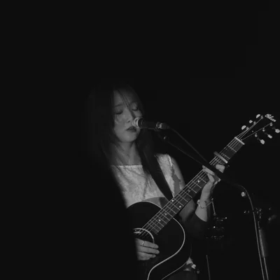 정우가 어쿠스틱 기타를 연주하면서 마이크 스탠드 앞에서 눈을 감고 노래를 부르고 있다.