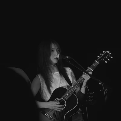 정우가 어쿠스틱 기타를 연주하면서 마이크 스탠드 앞에서 노래를 부르고 있다.