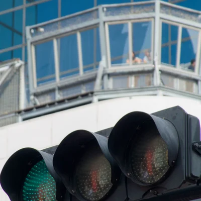 초록색 신호등에 초점이 맞춰져 있고, 그 너머에는 건물 전망대에 사람들이 서 있는 모습이 보인다.