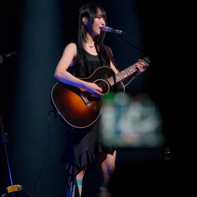 정우가 어쿠스틱 기타를 연주하며 노래를 부르고 있다. 관객석에는 그의 모습을 촬영하는 카메라의 디스플레이가 보인다.