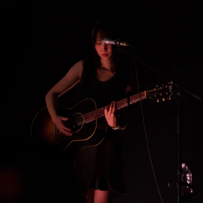 어둡고 붉은 조명 아래 정우가 어쿠스틱 기타를 연주하고 있다.